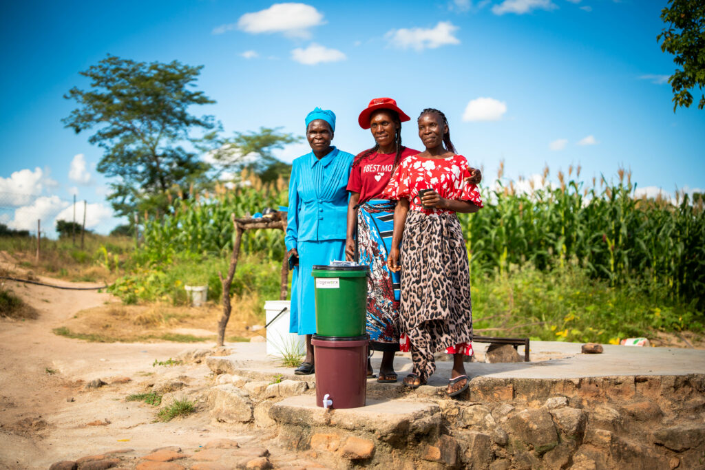three women standing with clean water after gaining access to a filter